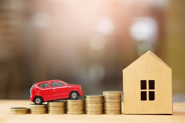 Photo of Saving money, Little toy car, money coins stacked on each other in different positions, house in paper model on the wooden table. Credit financial growing Loan to buy real asset concept.