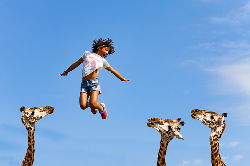 Happy carefree girl jump with giraffes heads bellow lifting hands and smile