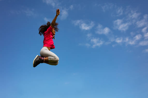 istock Happy curly girl jump pulling legs over clear sky 1176600615