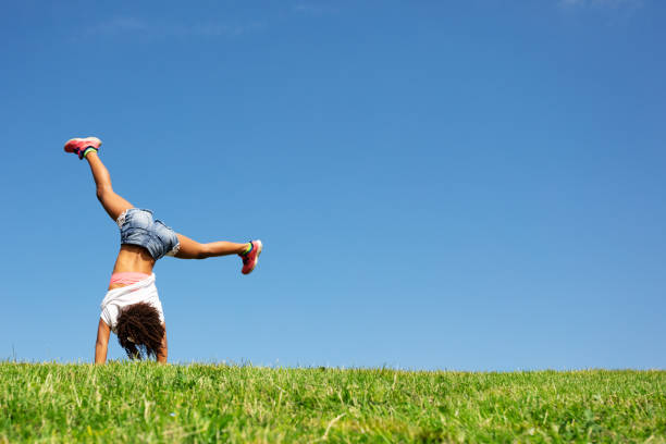 istock Young black girl stand on hands over sky from back 1176600679