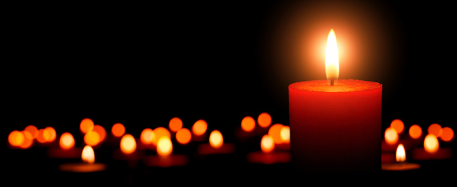 Low-key studio shot of elegant advent candles with one flame in the foreground, black background with defocused flames