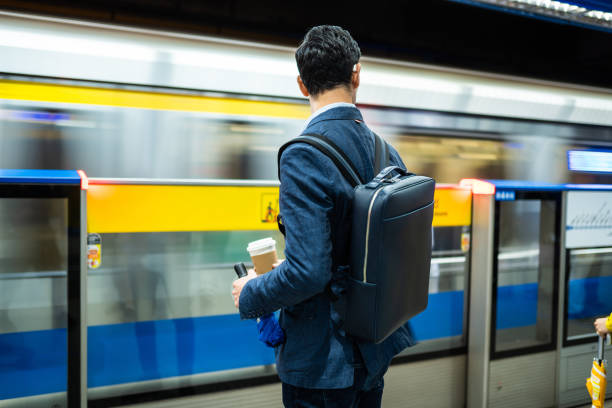 Waiting For Train At Subway Rear view of handsome man waiting fr train at subway, holding bag on his back and cup of coffee rush hour stock pictures, royalty-free photos & images