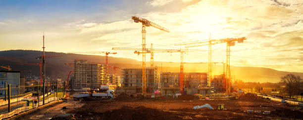 grande canteiro de obras que inclui diversos guindastes, com lotes da luz solar do ouro - construction equipment large construction crane - fotografias e filmes do acervo