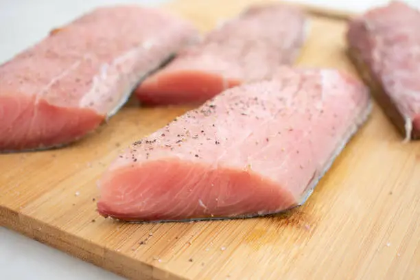 Raw fish fillets on a bamboo cutting board seasoned with salt and pepper