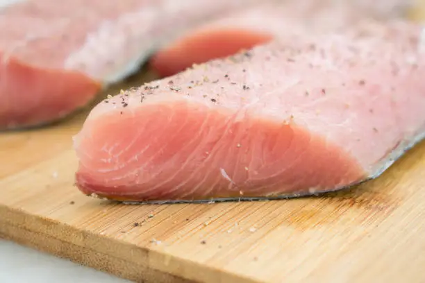Raw fish fillets on a bamboo cutting board seasoned with salt and pepper