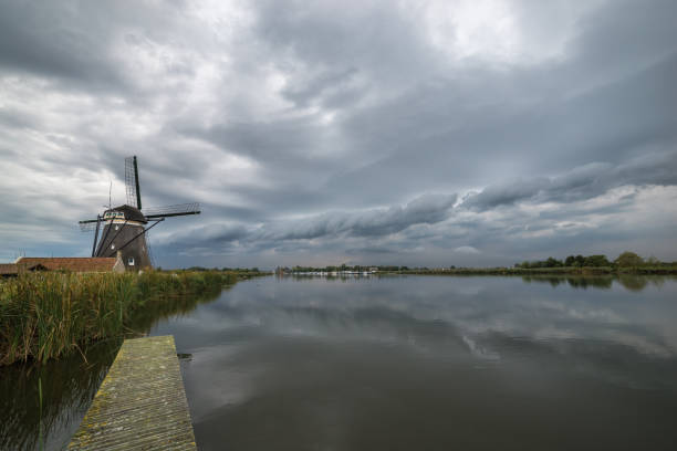 Scenic landscape image with classic dutch windmill and beautiful calm water before the storm.