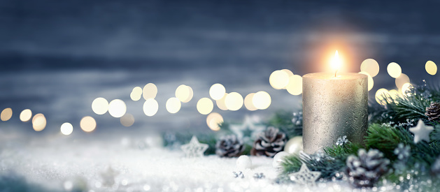 Christmas decoration with candle, lights, fir branches and ornaments on snow, panoramic format