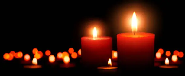 Low-key studio shot of elegant advent candles with two flames in the foreground, black background with defocused flames