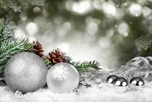 Glamorous Christmas scene with silver ornaments, fir branches and pine cones on snow and defocused lights in the background
