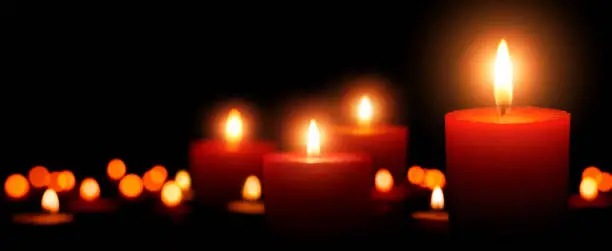 Low-key studio shot of elegant advent candles with four flames in the foreground, black background with defocused flames