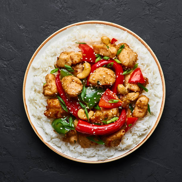 Schezwan Chicken or Dragon Chicken with basmati rice at black slate background. Szechuan Chicken is popular indo-chinese spicy dish with chilli peppers, chicken and vegetables.