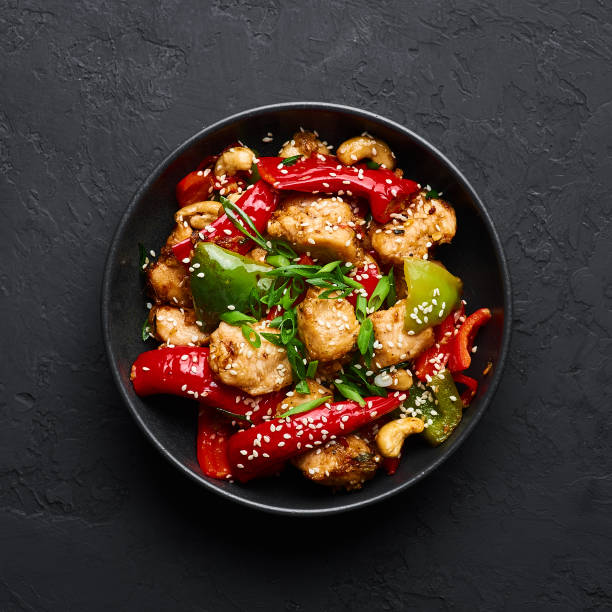 schezwan huhn oder drachenhuhn in schwarzer schüssel auf dunklem schiefer hintergrund. szechuan chicken ist ein beliebtes indo-chinesisches würziges gericht mit chilischoten, huhn und gemüse. - chinese cuisine stock-fotos und bilder