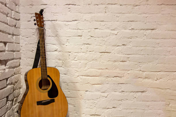 istock Guitar against white background. Acoustic musical instruments stands leaning on brick wall with empty copy space to add text of image. Music backdrop 1176613306