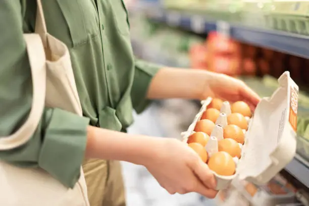 Photo of Girl at supermarket holding cotton shopper bag and buying eggs in craft package without plastic bags. Zero waste, plastic free concept. Sustainable lifestyle. Banner.