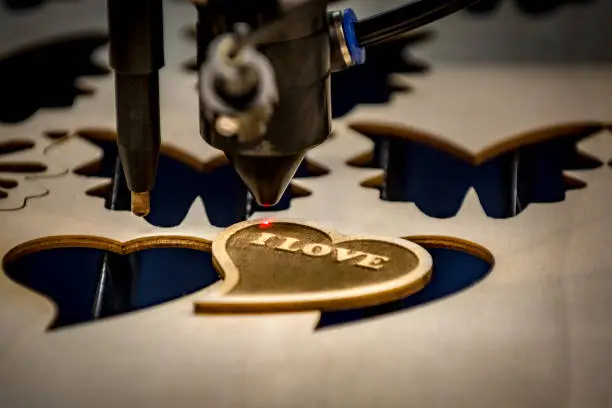 Close-up of laser engraving and cutting machine and just finished heart shaped wooden badge