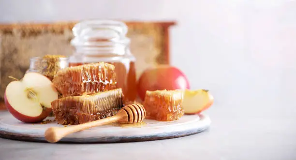 Apples with honey jar, honeycomb on grey background with copy space. Rosh hashanah jewish new year holiday celebration.