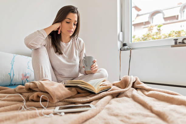 istock Woman drinking hot tea and reading book in bed 1176624408