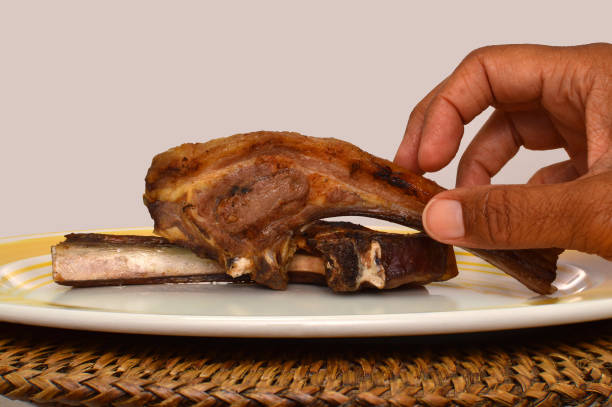 Hand grabbing barbecued lamp chop on plate