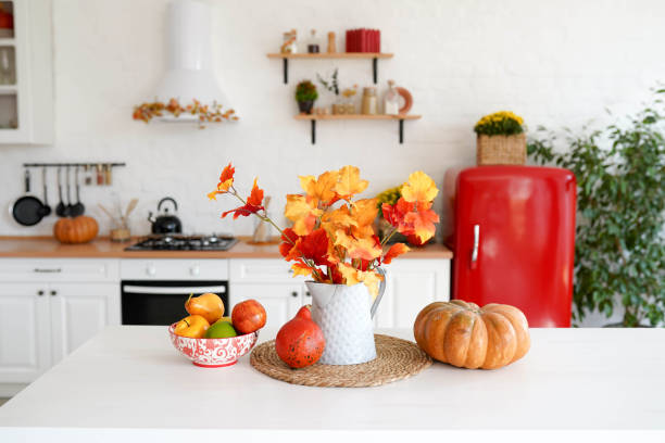 tavola autunnale con verdure in cucina. foglie rosse e gialle nel vaso e zucca su sfondo bianco. - autumn light leafes color image foto e immagini stock