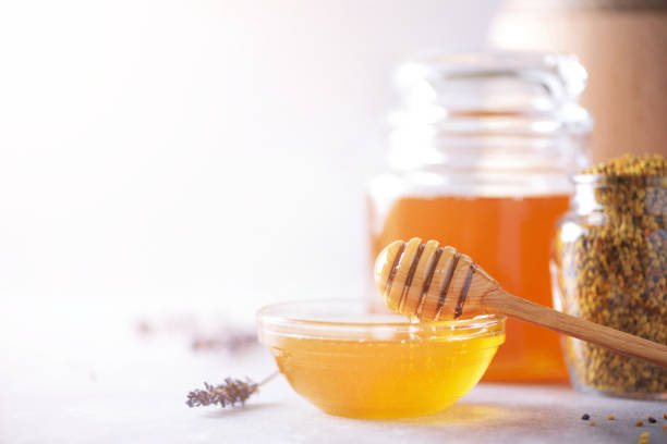 Bee pollen granules, honey jar with wooden dropper, honeycomb on grey backdrop. Copy space. Autumn harvest concept