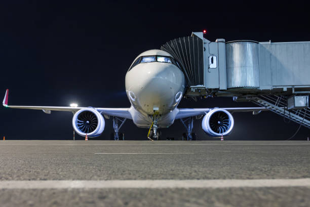 Front view of a white passenger aircraft connected to an external power supply on an airport night apron near the air bridge Front view of a white passenger airplane connected to an external power supply on an airport night apron near the air bridge passenger boarding bridge stock pictures, royalty-free photos & images