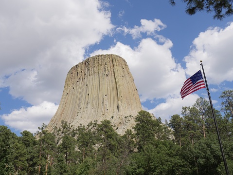 The Devils Tower  in Wyoming, America's first national monument, with breathtaking clouds in the skies and an American flag in the photo.