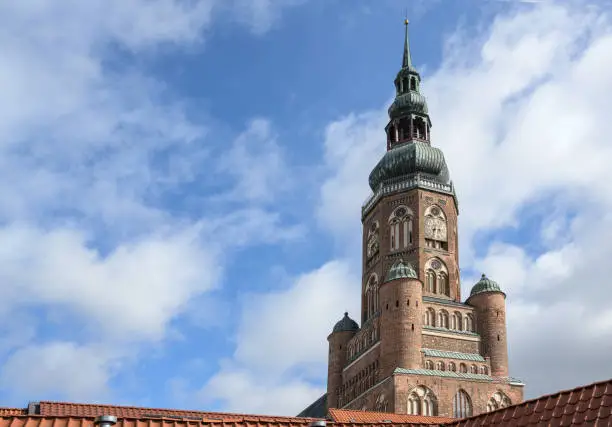 Tower of the St Nikolas church, cathedral of Greifswald over the roofs against a blue sky with clouds, copy space