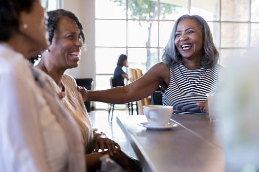 During their weekly coffee meeting, the three mature adult women share a laugh together.