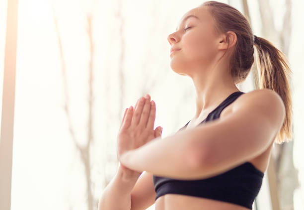 Low angle side view of woman putting palms together while doing yoga by window
