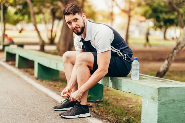 istock Young runner sitting in public park tying his shoelaces 1176665957