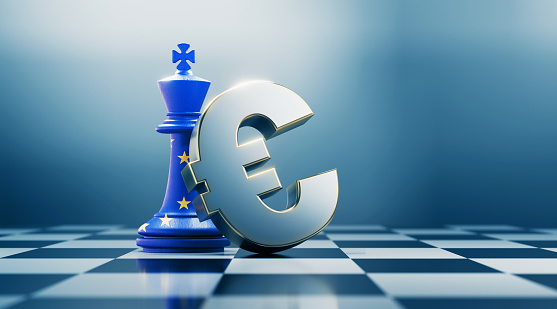 Single king chess piece and metallic Euro currency symbol are standing on black and white chessboard. King chess piece is textured with European Union flag. Horizontal composition with selective focus and copy space. Great use for Euro concepts.