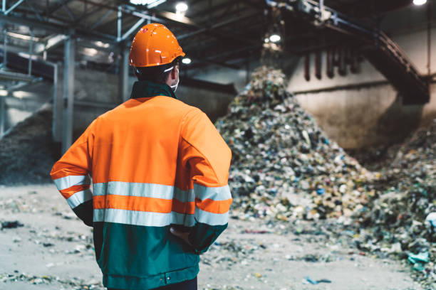 istock Worker in neon suit looking at piles of plastic waste 1176676583