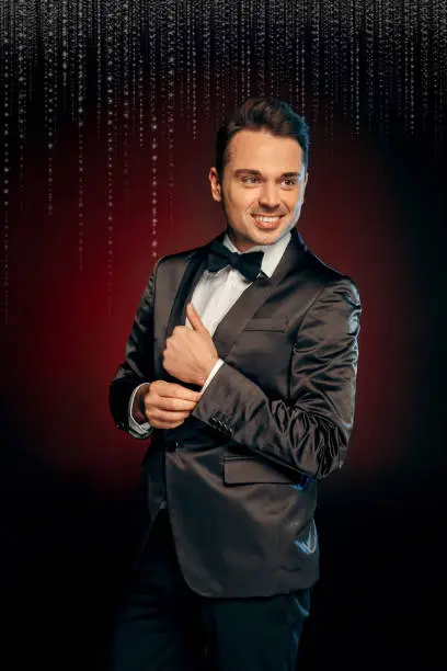 Professional showman wearing suit standing isolated on black and red background looking aside smiling happy