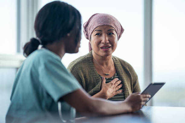 Asian woman with cancer meeting with female physician An Asian woman with cancer is consulting her doctor. The two women are seated at a table together. The patient is wearing a bandana to hide her hair loss. The medical professional is showing the patient test results on a digital tablet. They are discussing a treatment plan. chemotherapy drug stock pictures, royalty-free photos & images