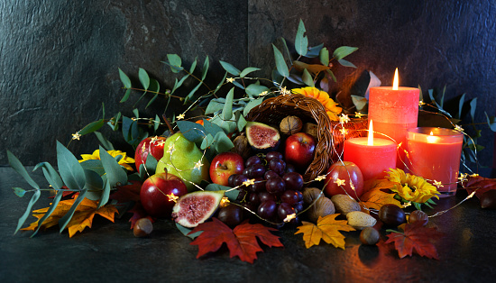 Happy Thanksgiving cornucopia table setting centerpiece decorated with autumn leaves, fruit, nuts and orange burning candles with copy space.Happy Thanksgiving cornucopia table setting centerpiece decorated with autumn leaves, fruit, nuts and orange burning candles, close up vertical.
