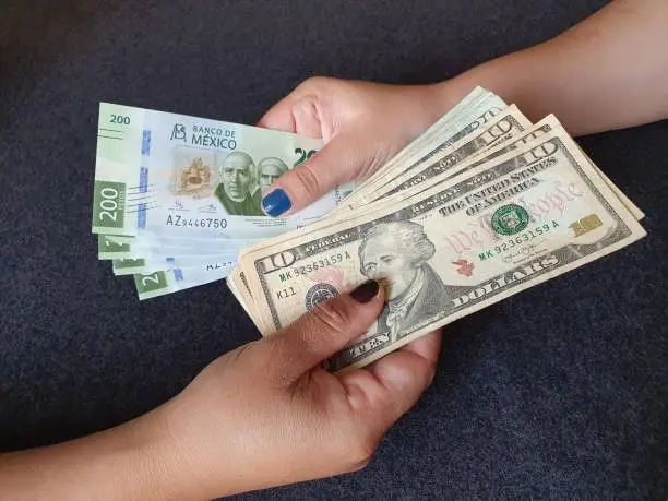 Photo of women hands exchanging Mexican banknotes and American dollar money