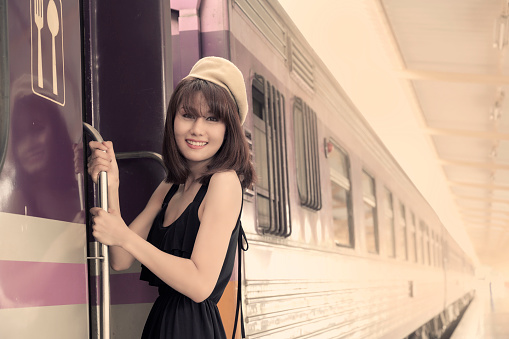 Beautiful young Asian woman tourist jumping on the train smiling, traveling concept