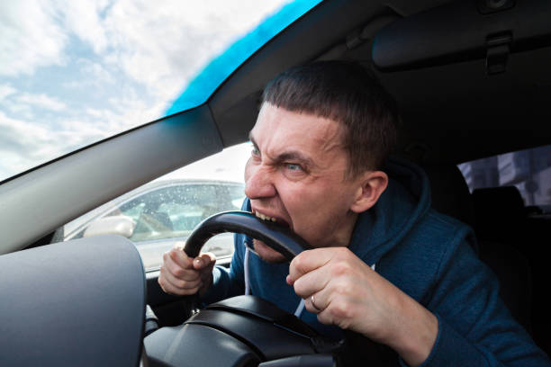 istock An unbalanced, goosey man bites a car steering wheel from anger while driving in a traffic jam or after an accident. A nervous and nutty guy cannot restrain his emotions and yells at other road users. 1176692861