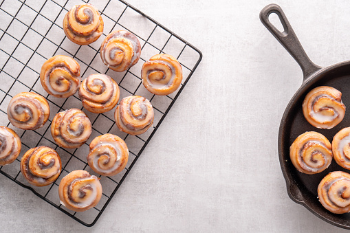 Homemade baked cinnamon rolls baked in an iron skillet cooling on cooling rack with icing
