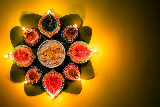 Photo of Happy Dussehra. Clay Diya lamps lit during Dussehra with yellow flowers, green leaf and rice on yellow pastel background. Dussehra Indian Festival concept.