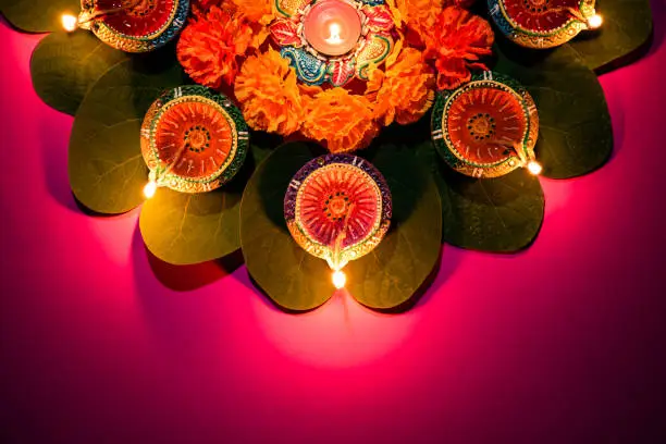 Photo of Happy Dussehra. Clay Diya lamps lit during Dussehra with yellow flowers, green leaf and rice on pink pastel background. Dussehra Indian Festival concept.