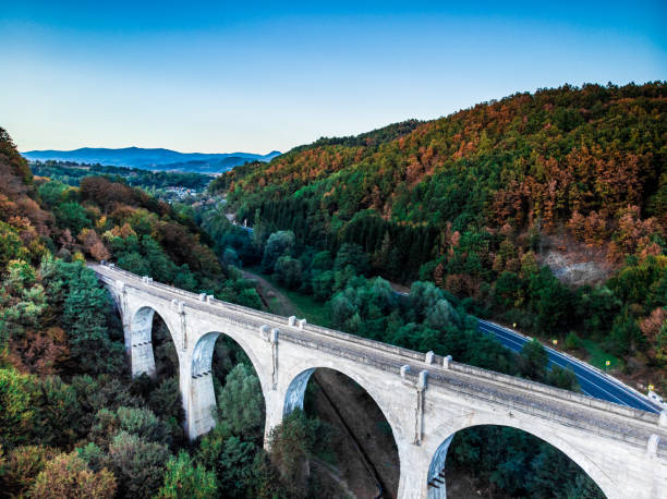 High angle color image taken with drone, depicting a highway with cars and other traffic, flanked by lush forest, and an old abandoned viaduct bridge. Room for copy space.