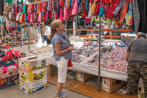 Alacati, Turkey - September 7th 2019: Senior woman looking at bandanas  on a market stall. The market is held every Saturday.