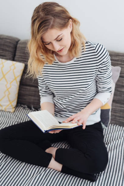 istock Young woman sitting cross-legged reading a book 1176711354