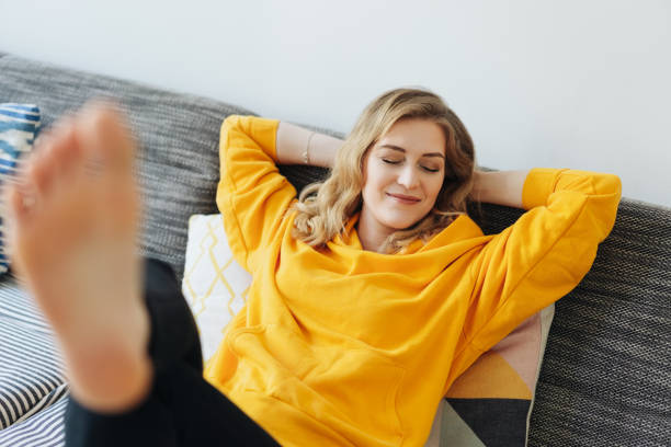 mulher nova descalça que relaxa com seus pés acima - divã sofá - fotografias e filmes do acervo