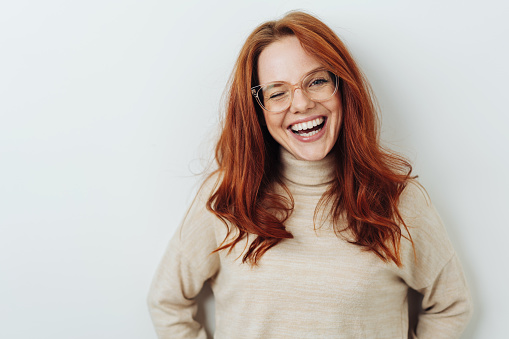 Laughing red-haired girl in glasses front close-up portrait against white wall with copy space