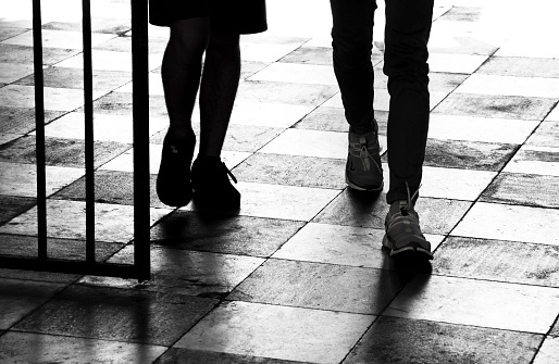 Silhouette shadow of two teenage boys walking through the gate; detail of legs in high contrast black and white