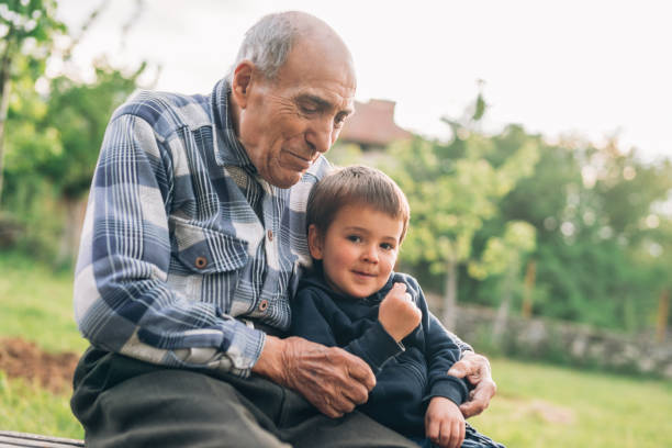 el abuelo se sienta en un banco y abraza a su lindo nieto. - great grandson fotografías e imágenes de stock