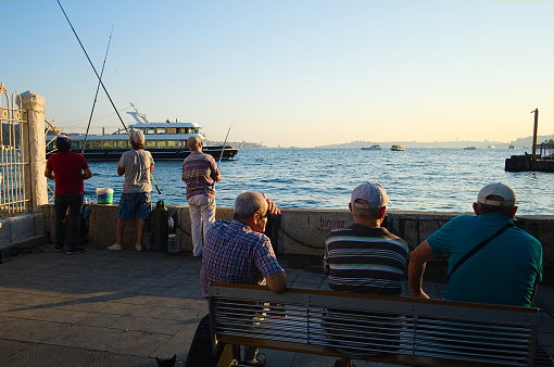 Istanbul, Turkey - September, 2018: Old men have rest and fishing on Ortakoy pier near Ortaköy Mosque building. Fishirmen on sunset in Istanbul.