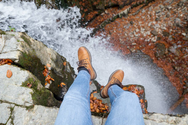 istock man legs in blue jeans and brown boots sitting on the edge looking at waterfall 1176723562